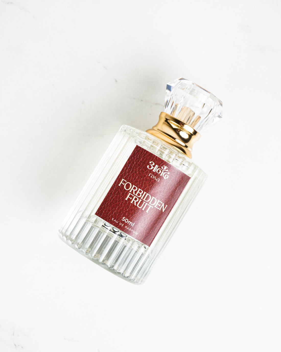 50ml Forbidden Fruit perfume by Sakura with clear ribbed glass bottle and gold cap on white marble background