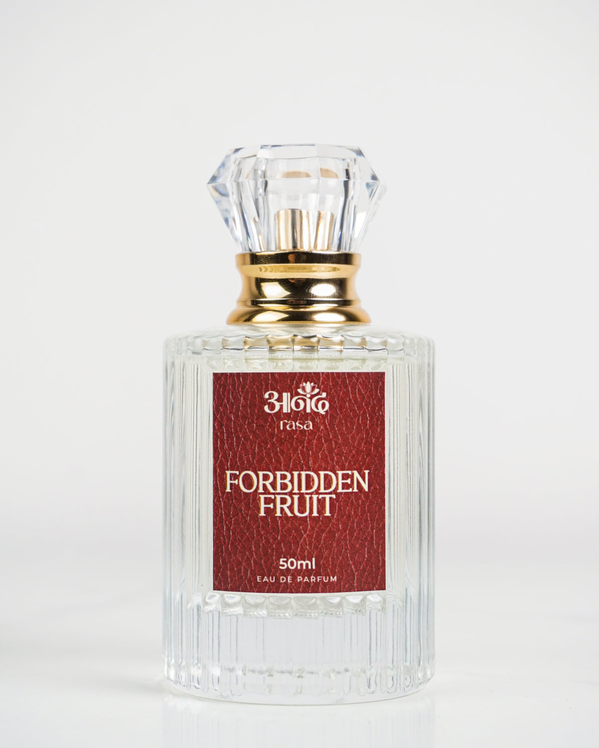 High-quality product image of Forbidden Fruit 50 ml perfume by Sakura, featuring a clear ribbed glass bottle, elegant gold cap and neck, and deep red textured label. The perfume bottle is photographed on a clean white marble background for a premium product presentation.