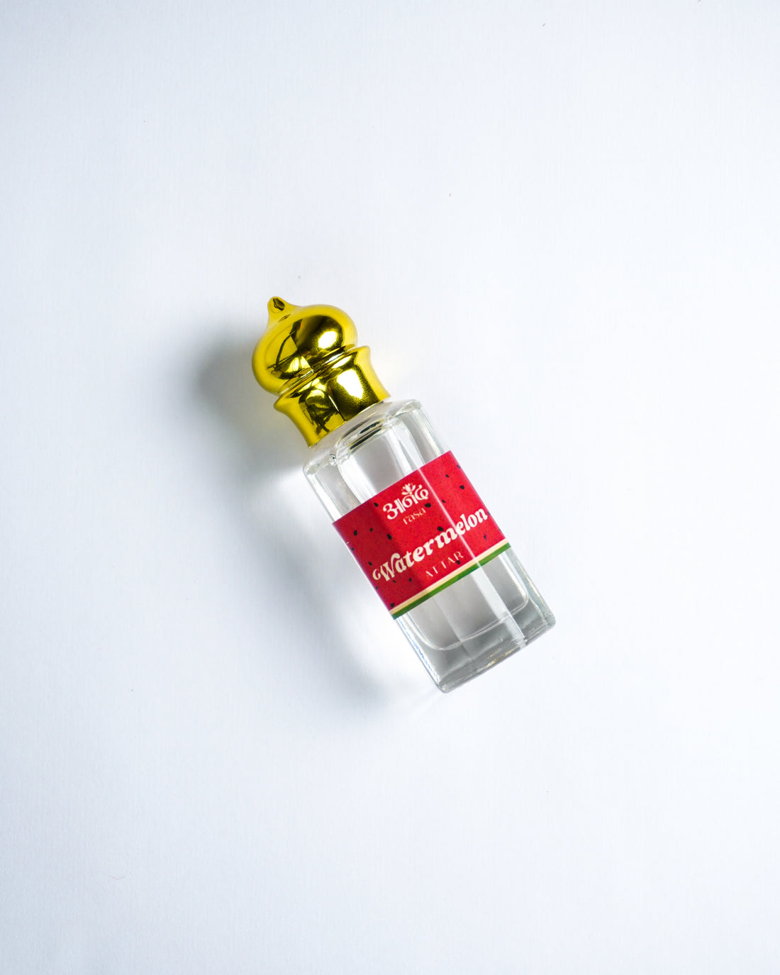 Ananda Rasa Watermelon Attar perfume bottle held in hand, surrounded by fresh watermelon slices in turquoise water.