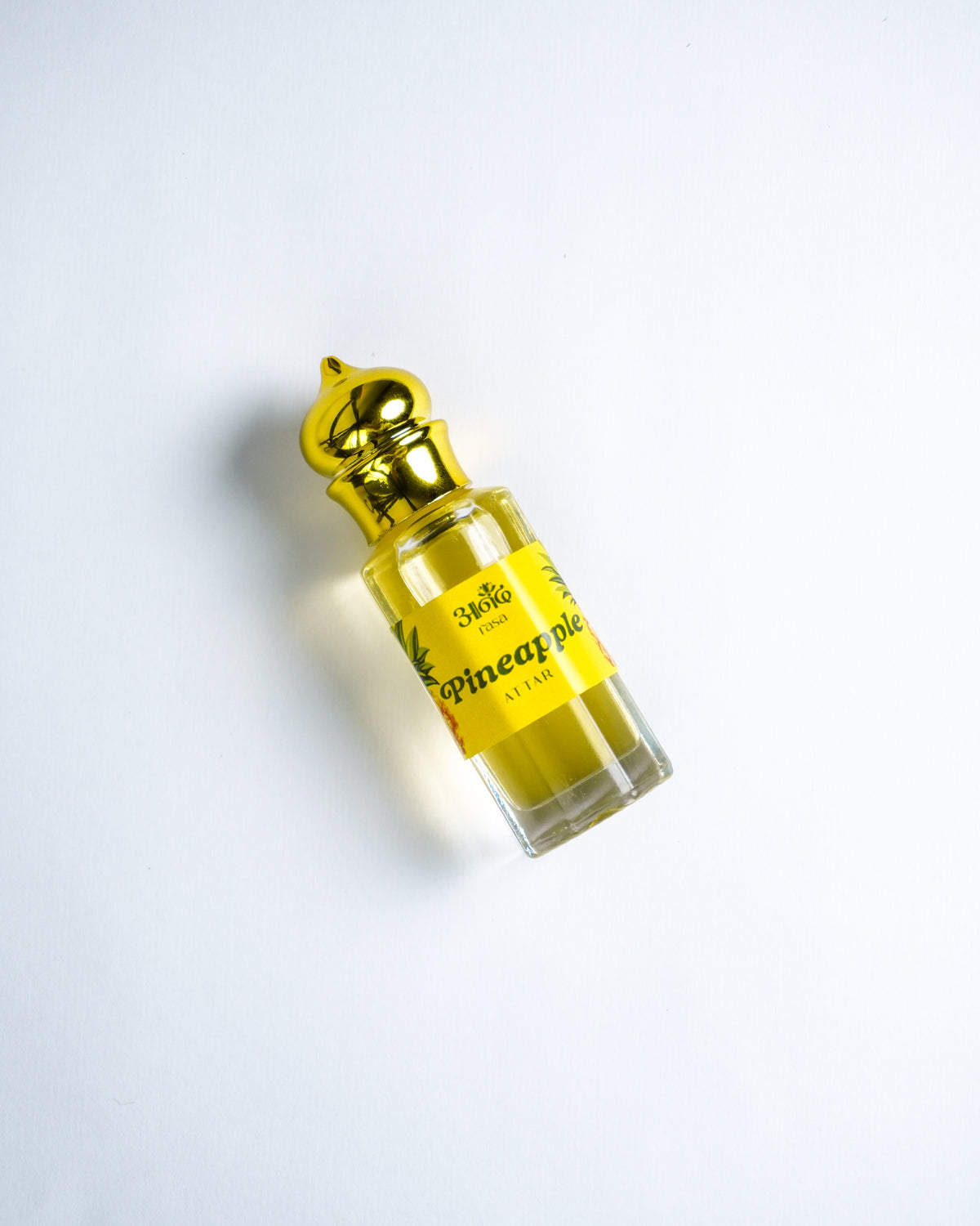Pineapple-scented attar perfume with fresh pineapple fruit on a vibrant red background
